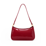 Glossy burgundy red women's shoulder bag with a long strap, zip closure and gold-tone hardware on a white background.